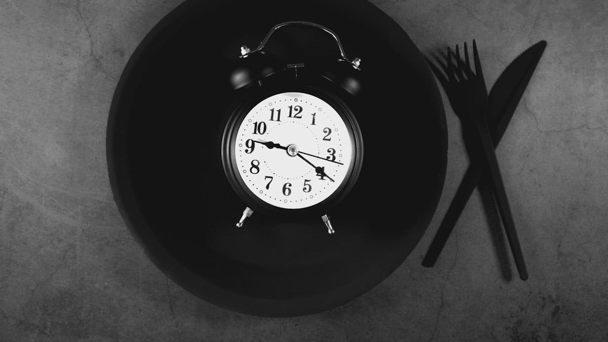 Alarm clock on black plate with cutlery on grey background