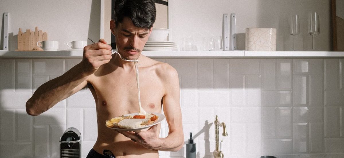 Young man enjoying a breakfast omelette in a sunlit kitchen setting.