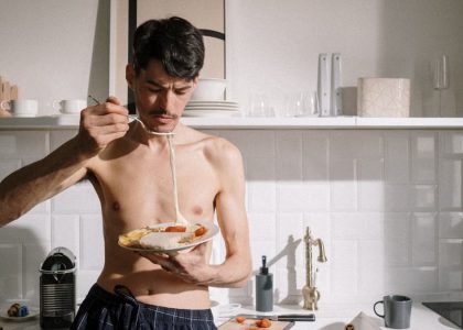 Young man enjoying a breakfast omelette in a sunlit kitchen setting.