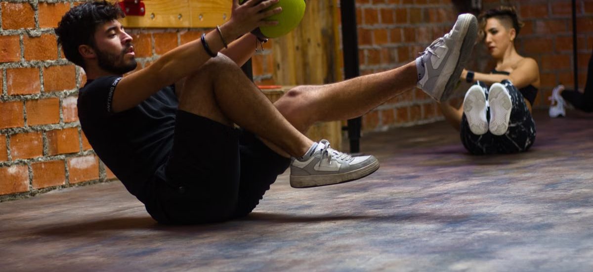 A man and woman perform core exercises with a medicine ball in a brick wall gym.
