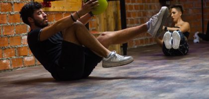 A man and woman perform core exercises with a medicine ball in a brick wall gym.