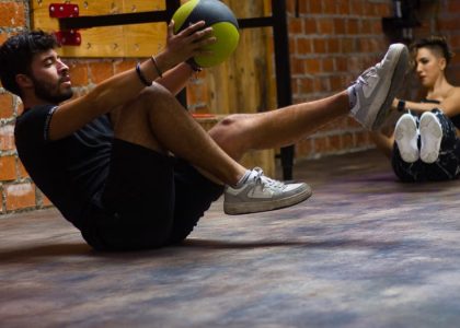 A man and woman perform core exercises with a medicine ball in a brick wall gym.